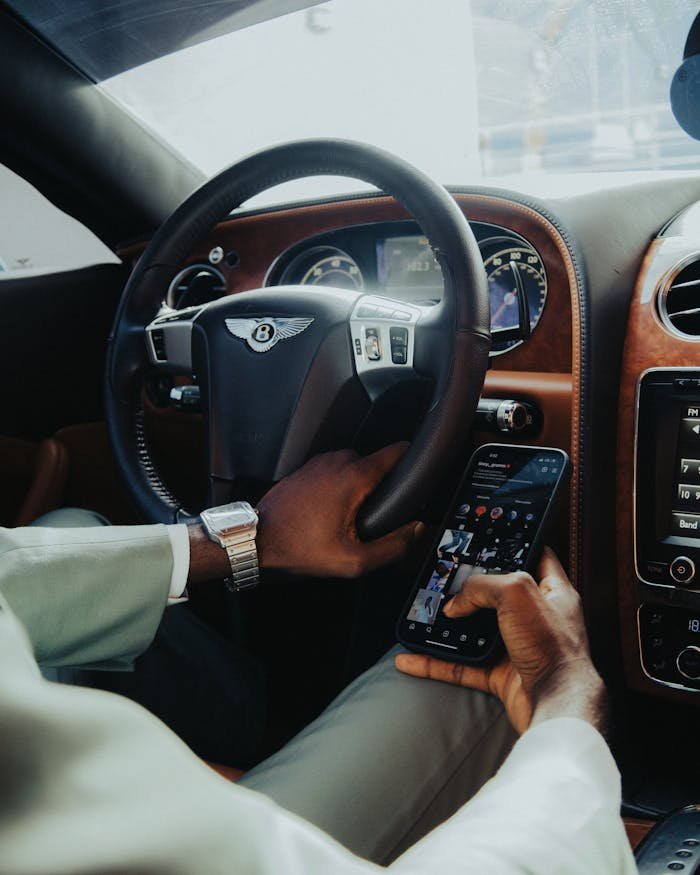 Close-up of a man using a smartphone while driving a luxury car, highlighting modern technology and design.