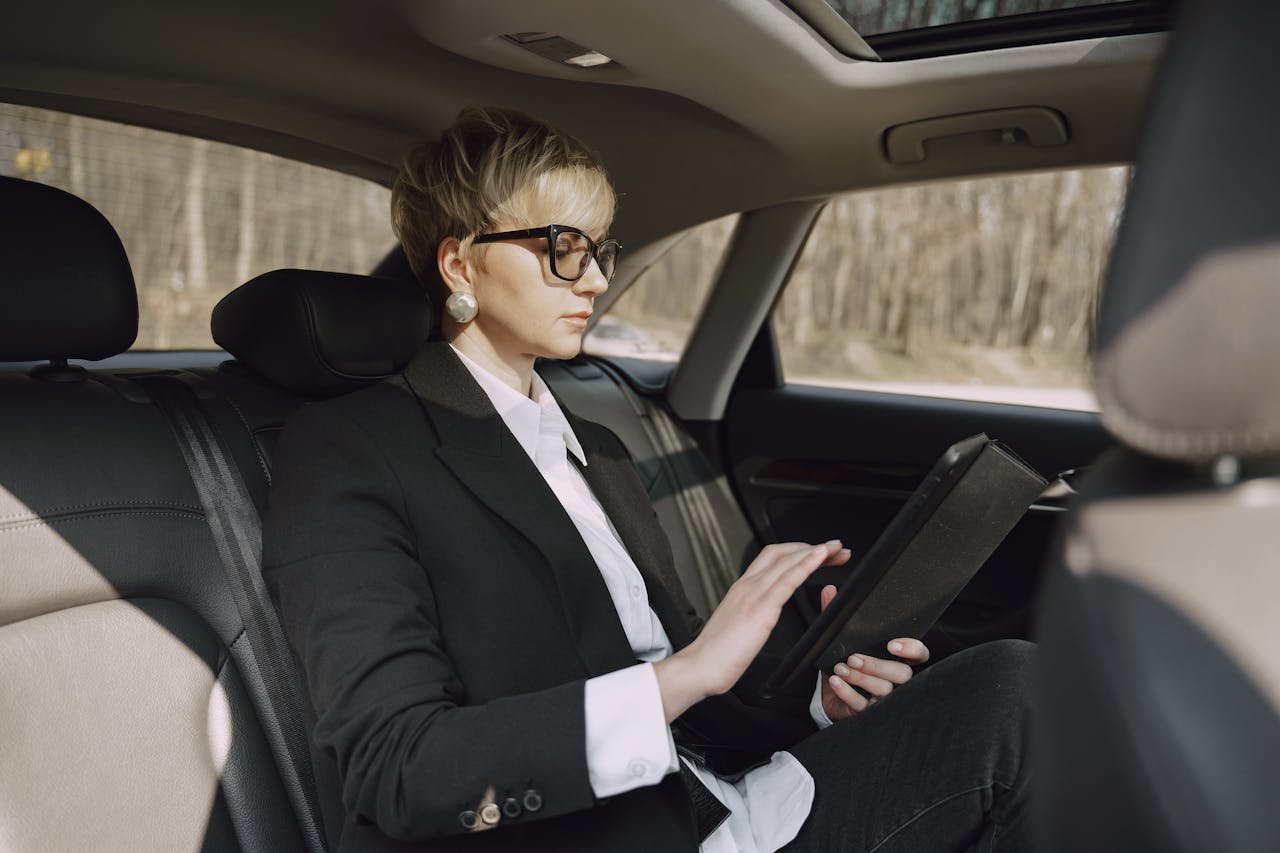 Side view of focused female in stylish formal clothes using tablet while riding on backseat of modern car