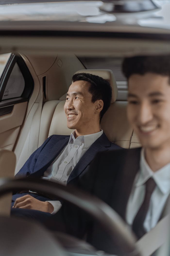 Two men in formalwear enjoying a comfortable ride in a luxury car, smiling.